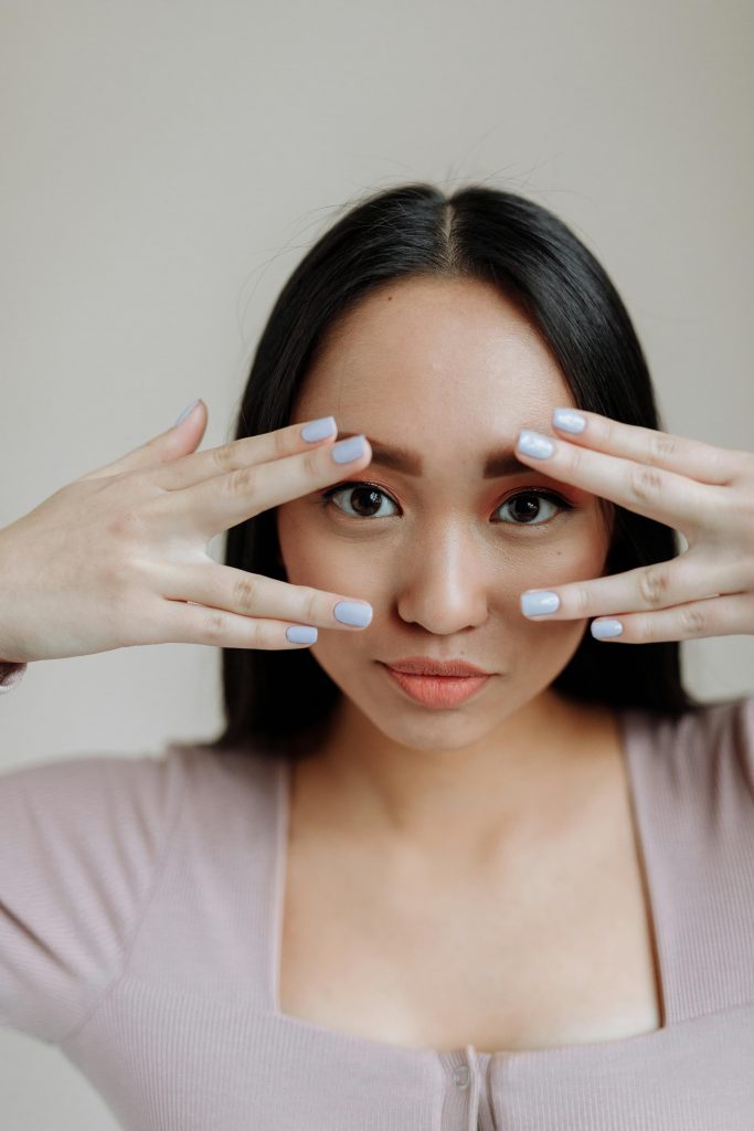 Eyes Close-up portrait of a young Asian woman framing her face with her hands, showcasing elegant simplicity.
