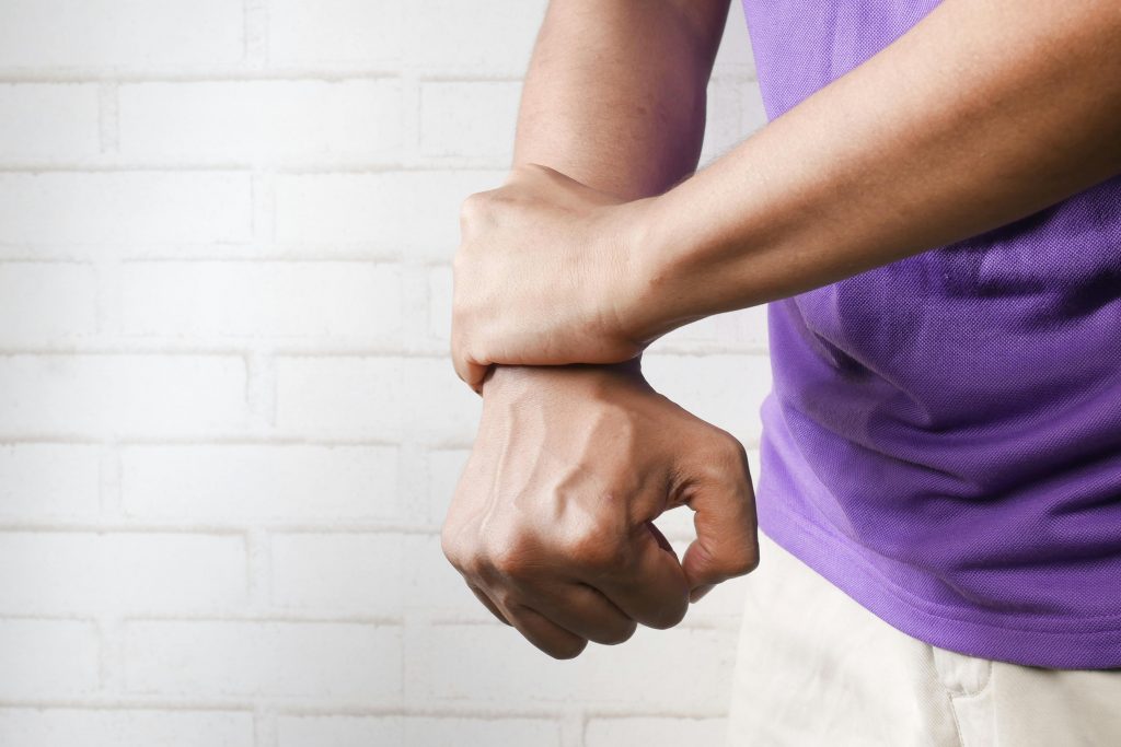 Close-up of a person holding their wrist in pain against a brick wall background.