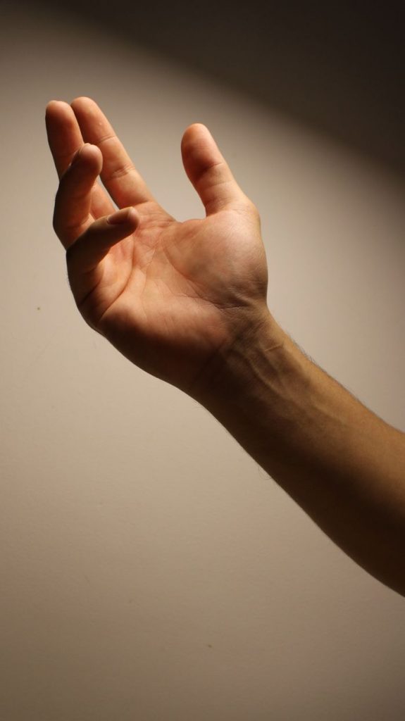 A close-up photo of an adult hand outstretched against dark to light gradient background
